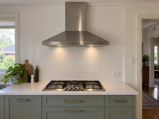 Stainless steel range hood above gas cooktop in a white tiled kitchen in Normanhurst
