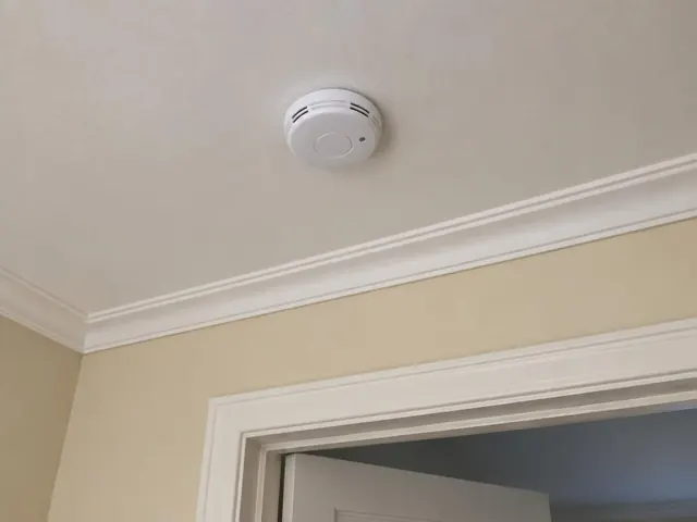 Smoke alarm on a cream ceiling above a hallway with white trim in Pennant Hills